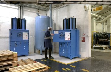 Trivium Packaging employee closing the door of a blue Mil-tek baler, with another blue baler visible in the background