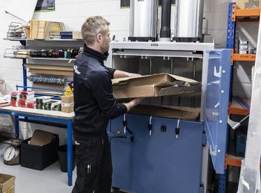 man in black clothes putting cardboard in a recycling compactor with the text A406