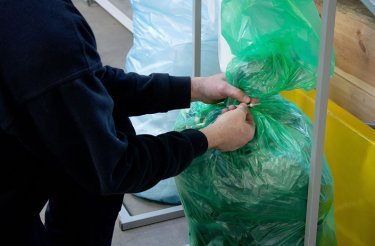 man handles a green infinity waste bag hygienically